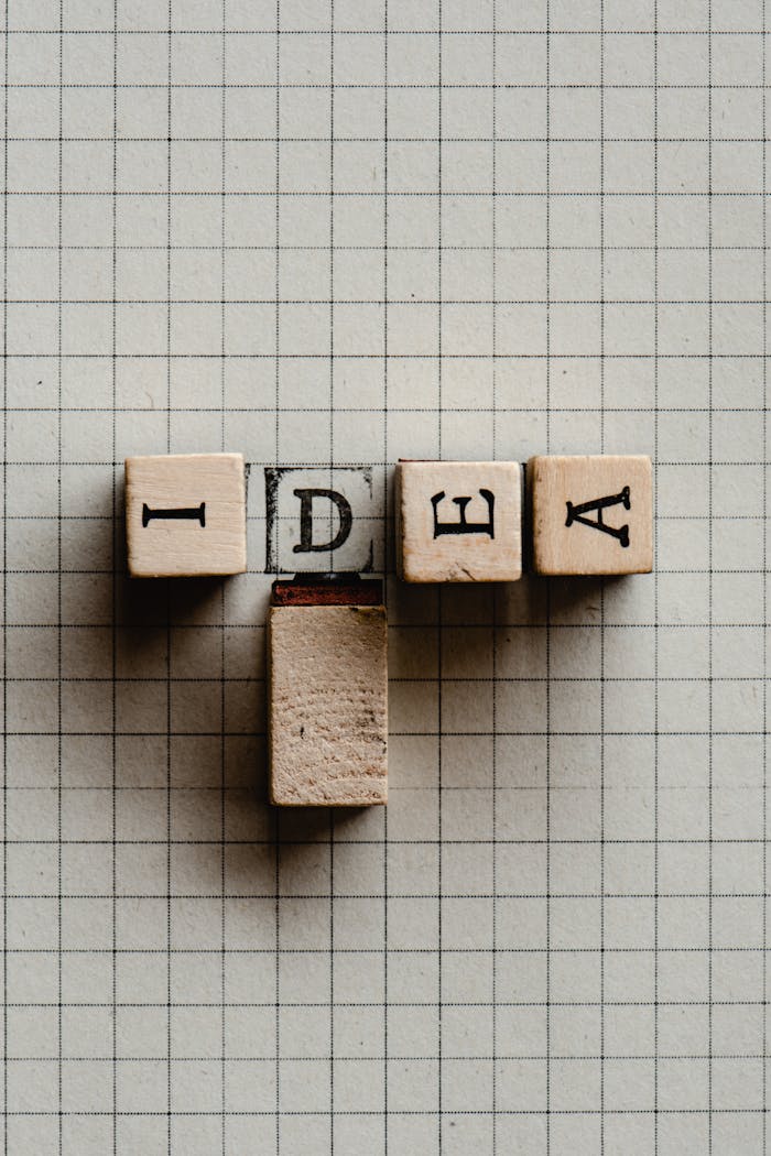 Close-up of wooden letter tiles spelling 'IDEA' on graph paper.
